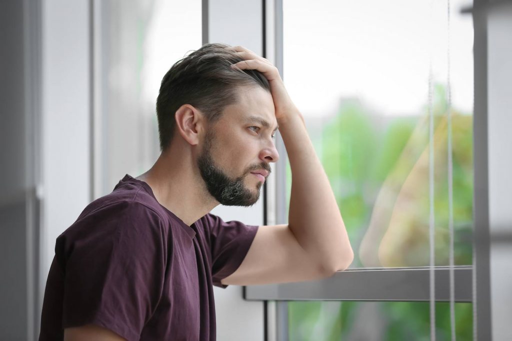 Ein Mann mit psychischer Erkrankung schaut aus dem Fenster und denkt über eine Reha nach